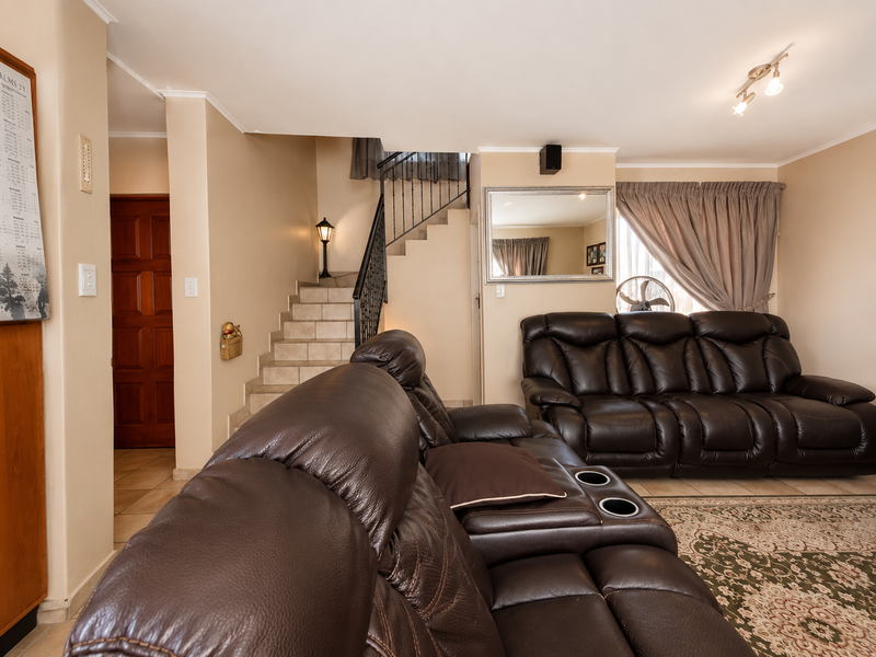 A comfortable living room featuring a staircase with a wrought iron balustrade, neutral wall tones, and tiled flooring throughout the space.