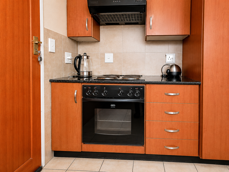 A compact kitchen featuring wooden cabinetry, a built-in Defy oven with electric hob, extractor fan, and tiled backsplash with granite countertops.