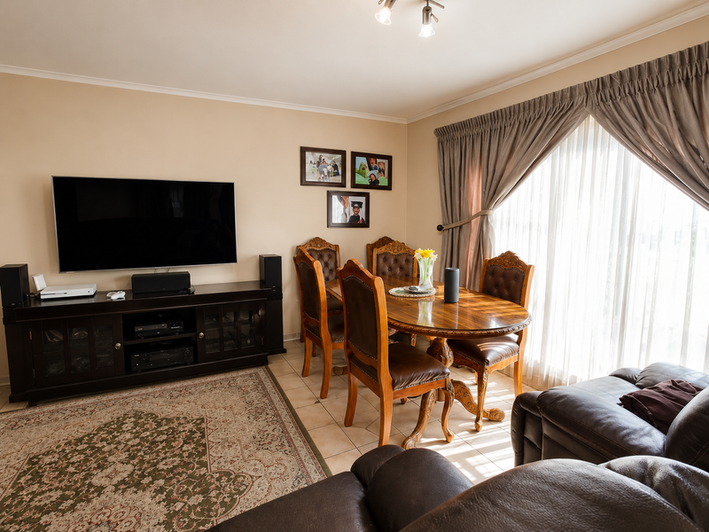 A well-maintained living and dining area featuring tiled flooring, neutral wall tones, and large windows with integrated curtain tracks.