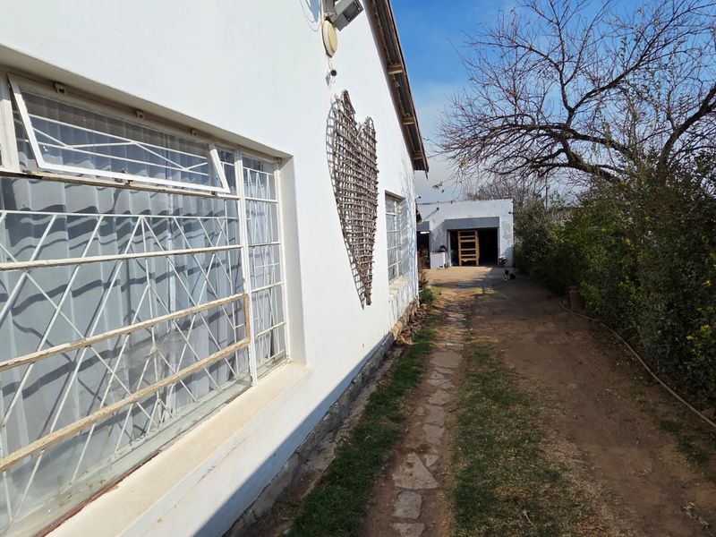 A view of the rear exterior of the property featuring a stone pathway, security-barred windows, and a detached garage in the background.