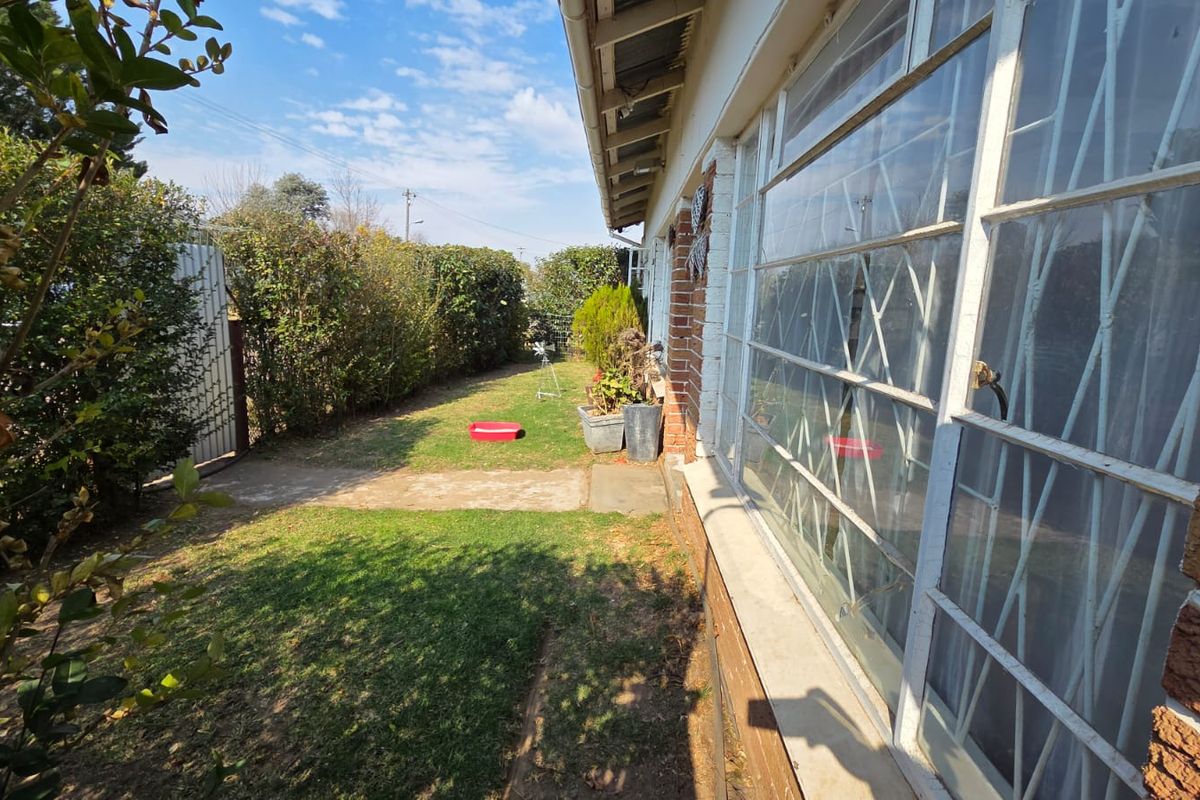 A view of the rear garden area featuring a concrete pathway, established hedging, and the rear brick facade of the house with security bars.