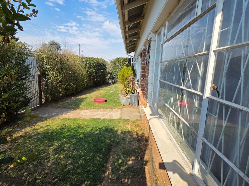 A view of the rear garden area featuring a concrete pathway, established hedging, and the rear brick facade of the house with security bars.