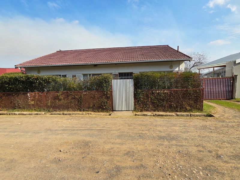 Front exterior view of a single-story house featuring a tiled roof, metal gate, and wire mesh fencing with an adjacent garage.