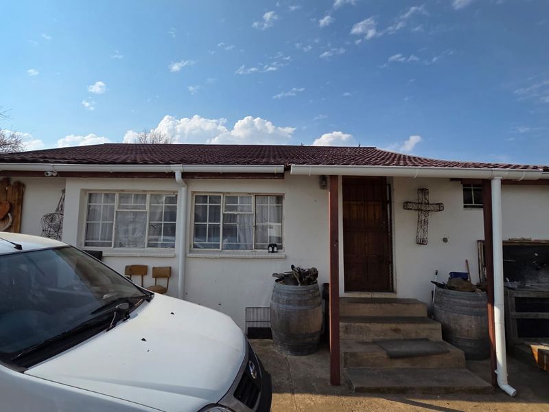 Rear exterior view of the house featuring a tiled roof, concrete entrance steps, and a built-in braai area.