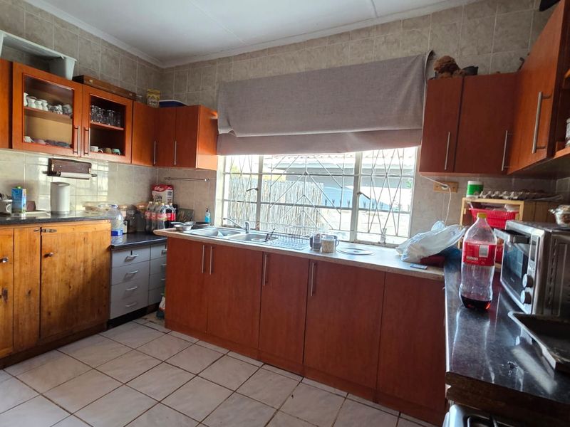A functional kitchen featuring wooden cabinetry, tiled splashbacks, and a double basin sink with a window overlooking the exterior.
