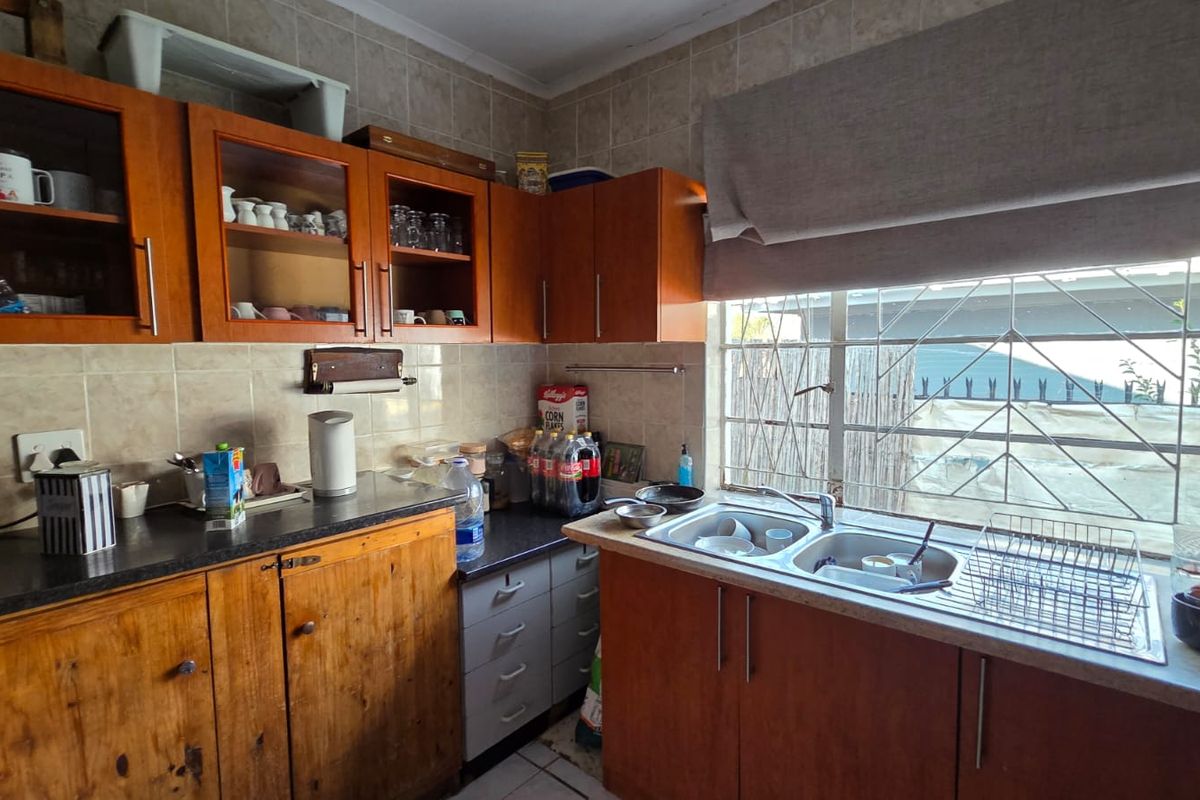 A functional kitchen featuring wooden cabinetry, laminate countertops, a double bowl stainless steel sink, and tiled backsplash with security bars on the window.