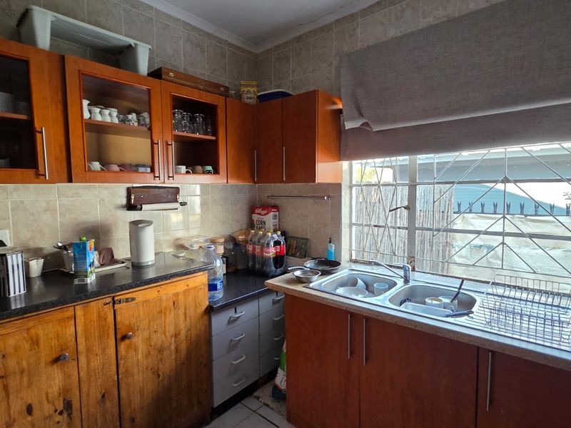 A functional kitchen featuring wooden cabinetry, laminate countertops, a double bowl stainless steel sink, and tiled backsplash with security bars on the window.