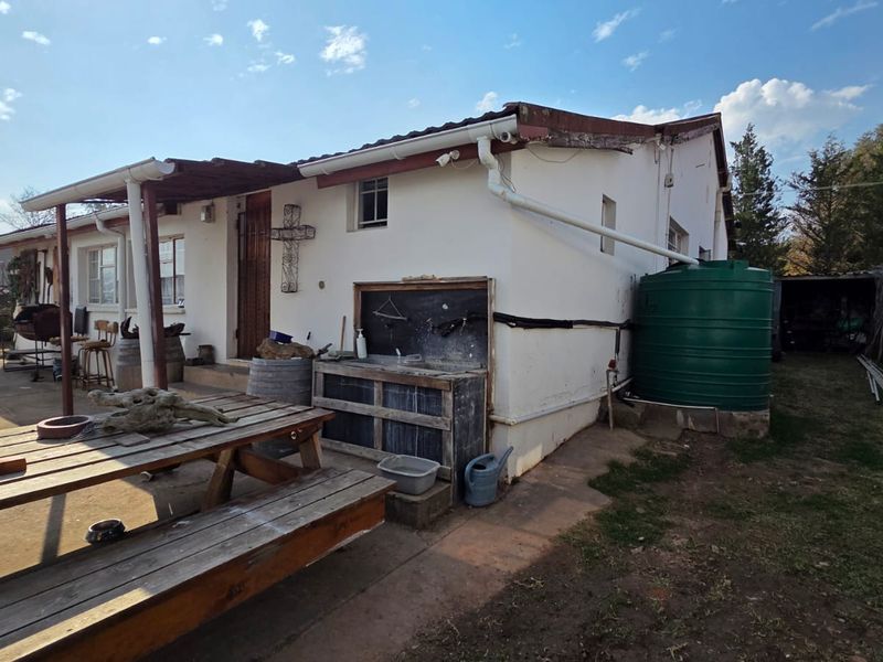 Rear exterior view of the house featuring a covered patio area, external wash basin, and a large water storage tank connected to the gutter system.