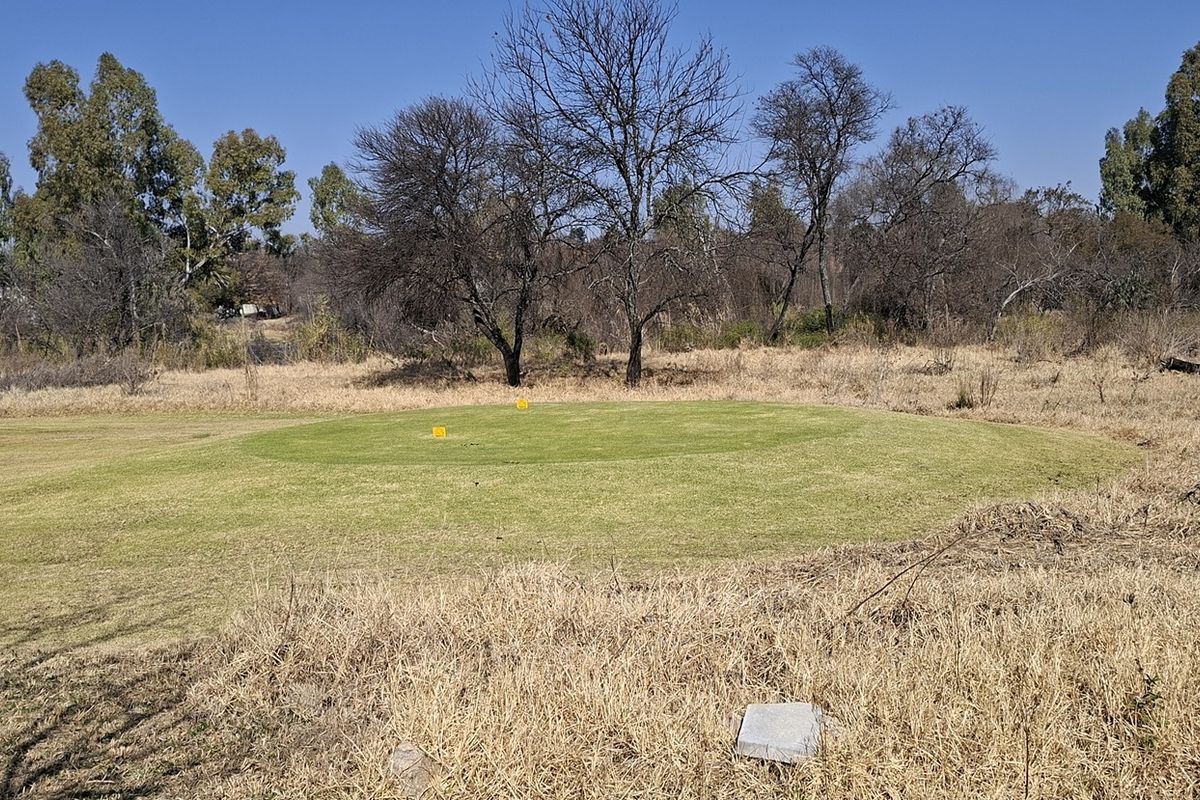 A view of a vacant residential plot featuring a maintained grassy area surrounded by mature trees and natural dry vegetation.