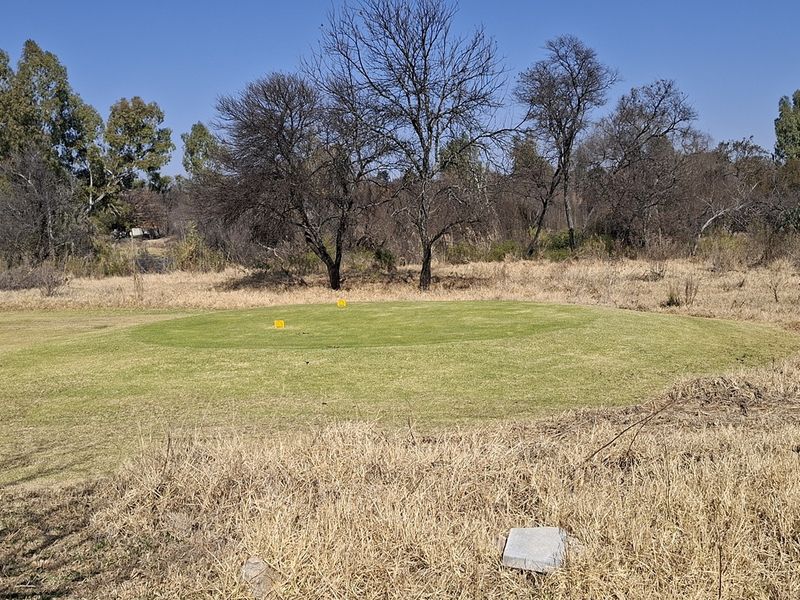 A view of a vacant residential plot featuring a maintained grassy area surrounded by mature trees and natural dry vegetation.