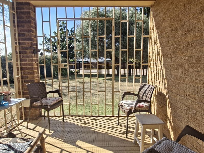 A covered patio area featuring brick walls, tiled flooring, and secure metal security bars overlooking the garden.