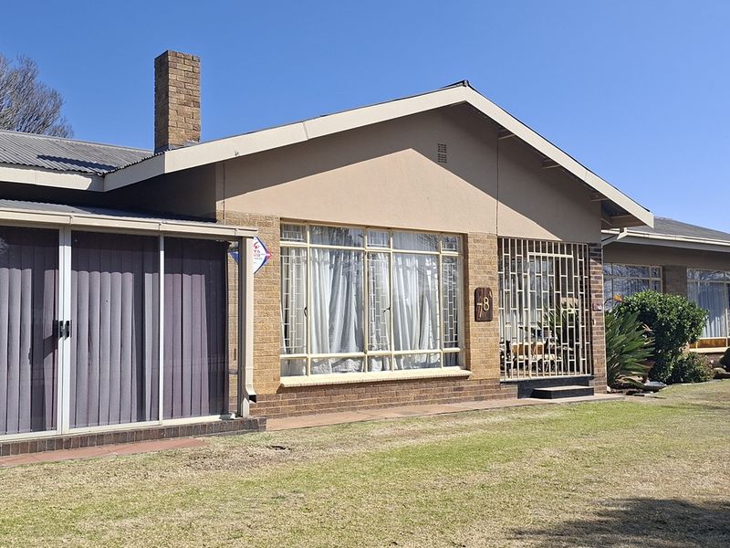 Front elevation of a single-story brick house featuring a corrugated metal roof, enclosed patio area, and security bars on windows.