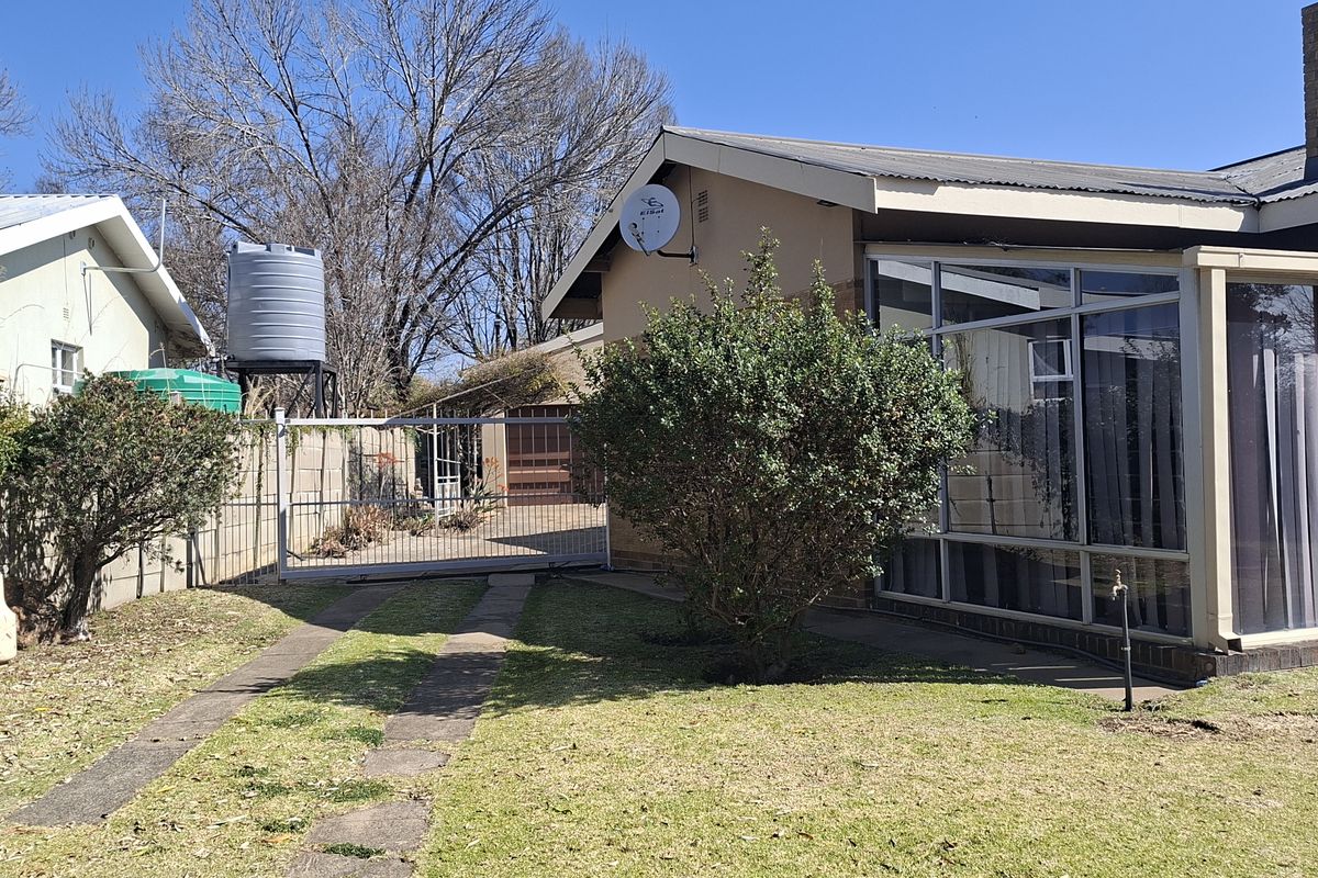 Rear view of the property featuring an enclosed patio, a brick chimney, a water tank, and a gated driveway with a surrounding boundary wall.