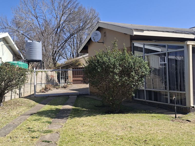 Rear view of the property featuring an enclosed patio, a brick chimney, a water tank, and a gated driveway with a surrounding boundary wall.