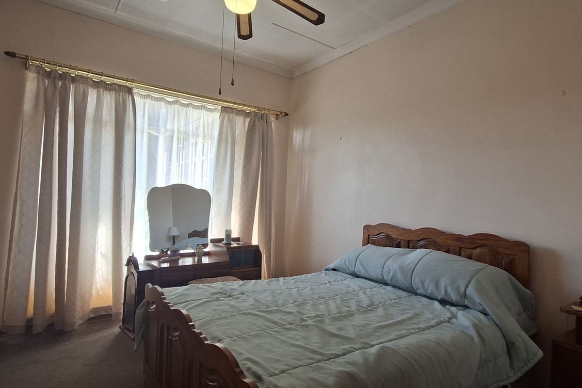 A standard bedroom featuring built-in cupboards, a ceiling fan, and large windows with curtain rails, offering a functional and well-lit living space.