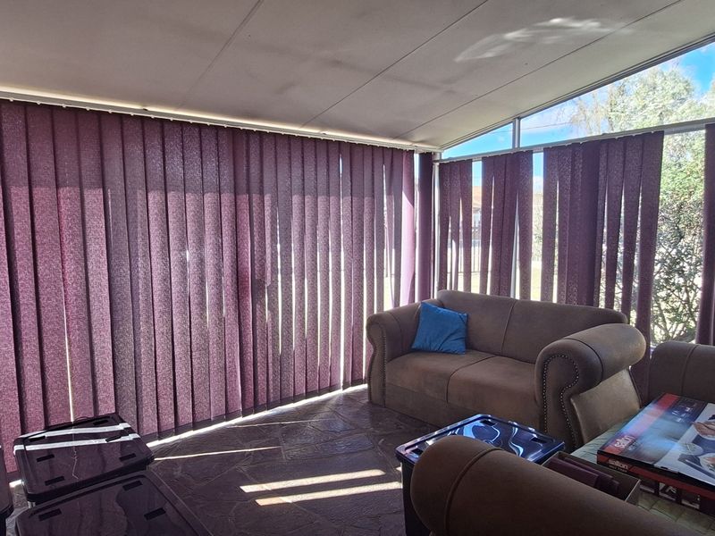Enclosed patio area featuring stone flooring and extensive glass windows with vertical blinds, offering a bright and versatile space.