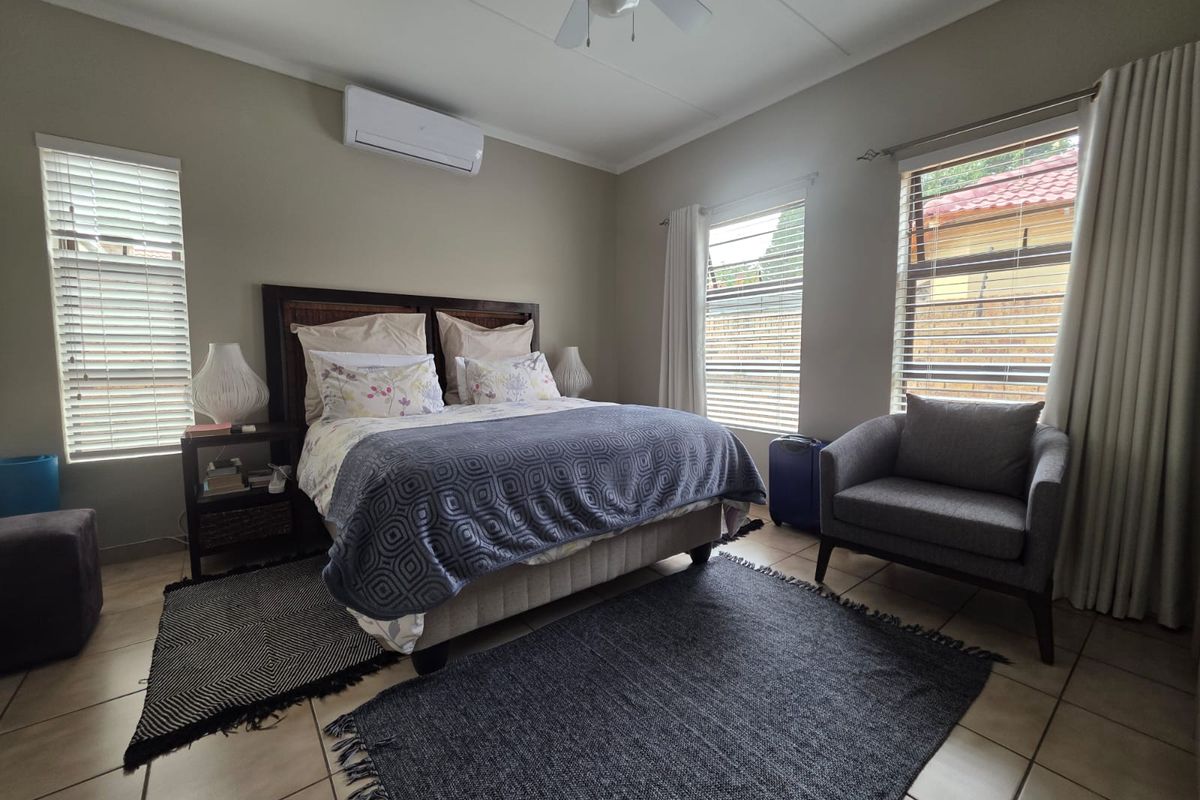A well-maintained bedroom featuring tiled flooring, a ceiling fan, and a wall-mounted air conditioning unit with natural light from multiple windows.