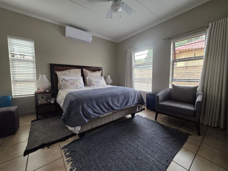 A well-maintained bedroom featuring tiled flooring, a ceiling fan, and a wall-mounted air conditioning unit with natural light from multiple windows.