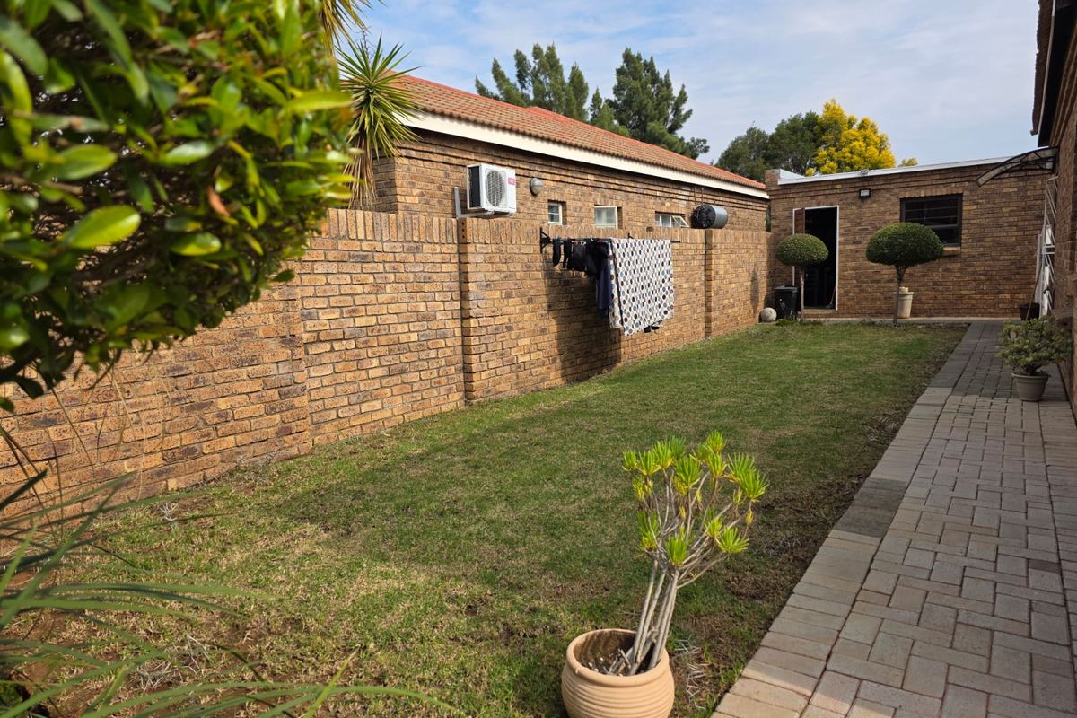 A private rear garden featuring a brick boundary wall, a paved walkway, and a well-maintained lawn area.