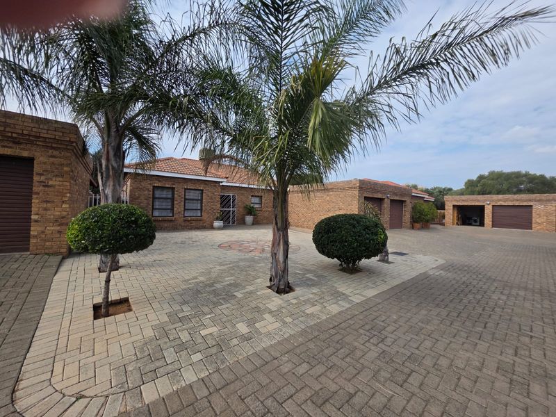 A well-maintained townhouse exterior featuring a spacious paved driveway, brick facade, and multiple garage access points.