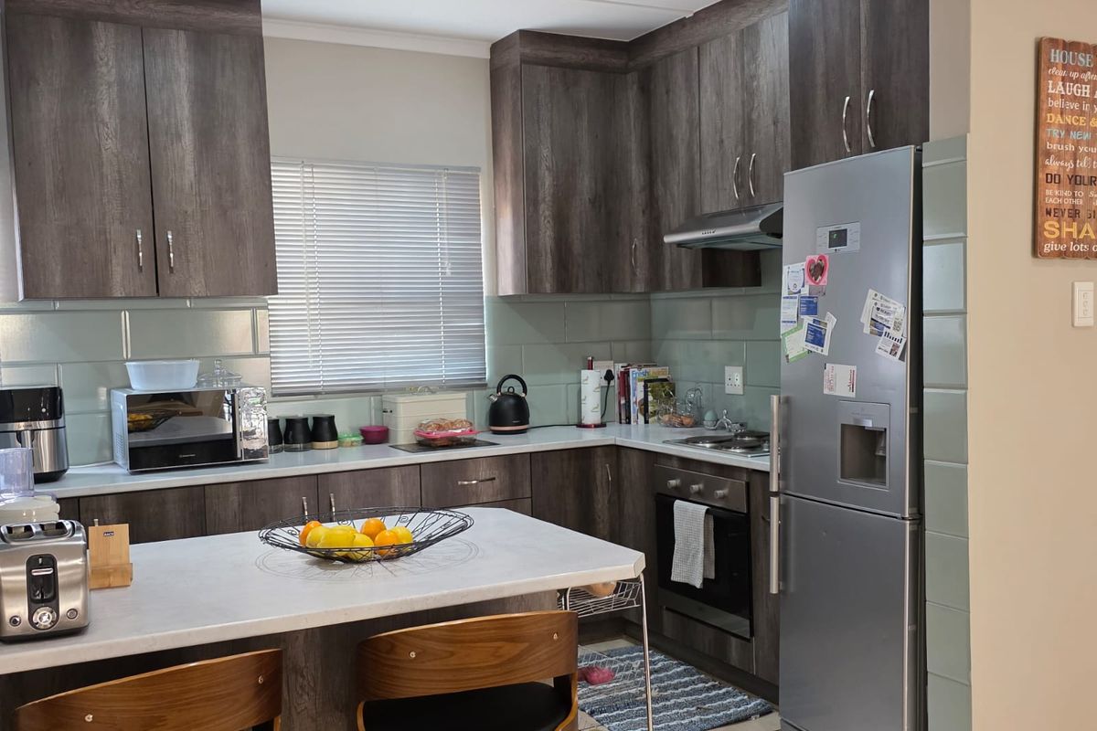 A functional kitchen featuring dark wood-look cabinetry, light countertops, a built-in oven with hob, and a tiled backsplash with integrated lighting.