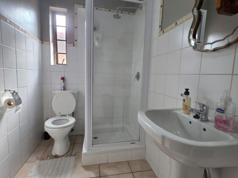 A functional bathroom featuring a pedestal basin, a glass-enclosed shower, and a toilet, finished with neutral wall and floor tiling.