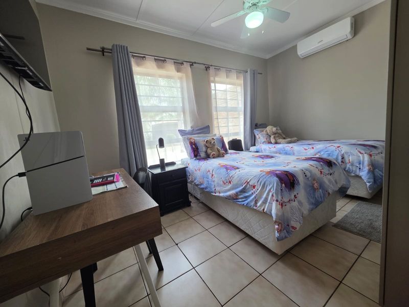 A functional bedroom featuring tiled flooring, a ceiling fan, and a wall-mounted split-system air conditioner.