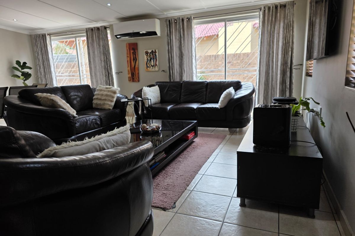 A well-maintained living room featuring tiled flooring, a split-system air conditioner, and large sliding glass doors with security gates providing natural light.