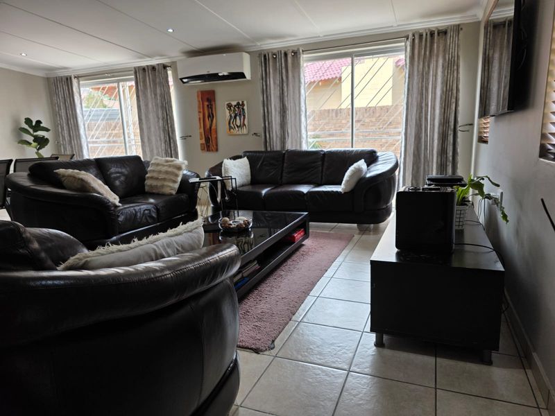 A well-maintained living room featuring tiled flooring, a split-system air conditioner, and large sliding glass doors with security gates providing natural light.