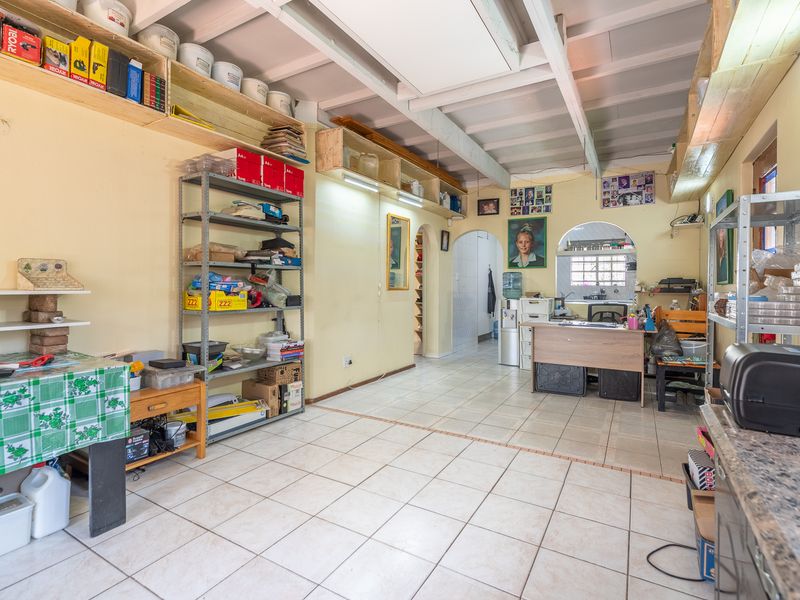 A functional utility space featuring ceramic tiled flooring, exposed beam ceilings, and built-in wall shelving, currently utilized as a workspace.