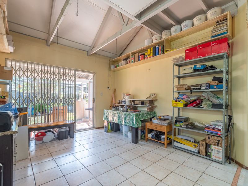 A functional garage space featuring tiled flooring, exposed rafters, and extensive built-in wall shelving, with direct access to the rear garden via a security gate.