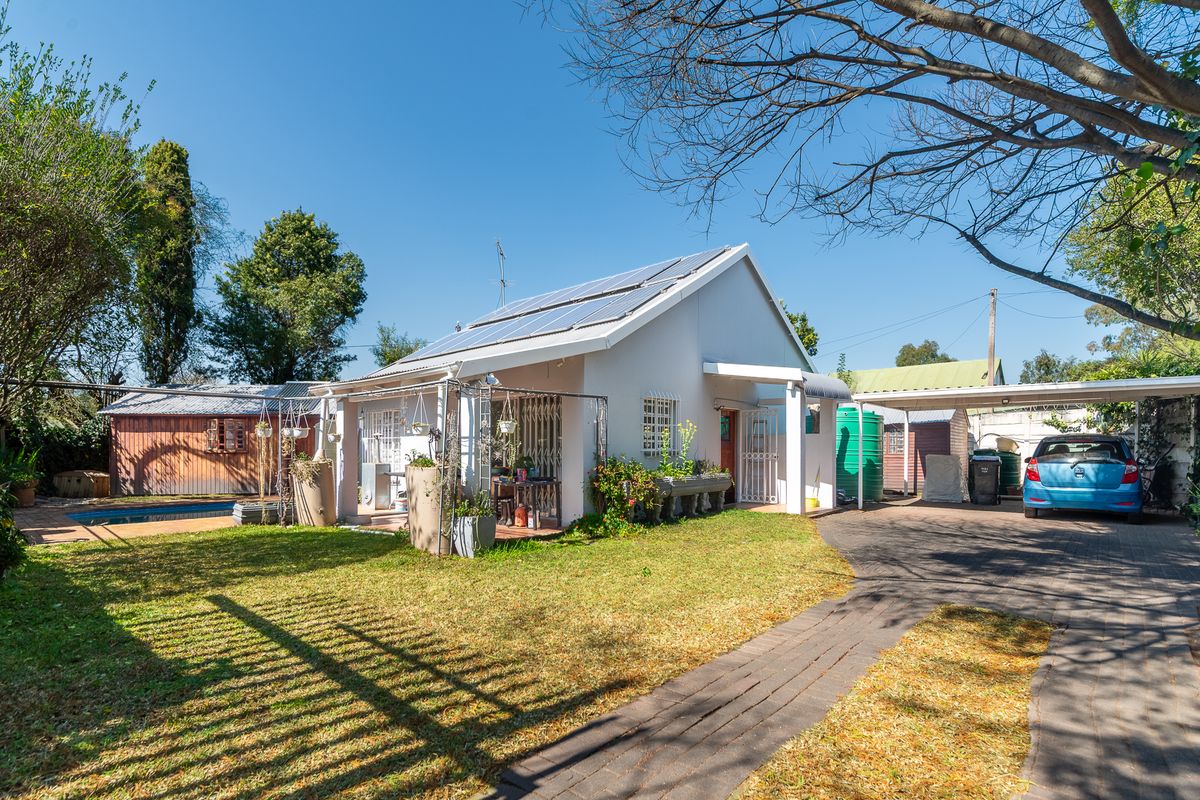 Rear view of the property featuring a paved driveway, carport, swimming pool, solar panels, and a garden area with a timber shed.
