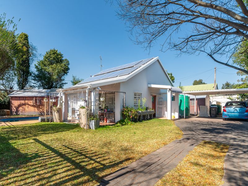 Rear view of the property featuring a paved driveway, carport, swimming pool, solar panels, and a garden area with a timber shed.