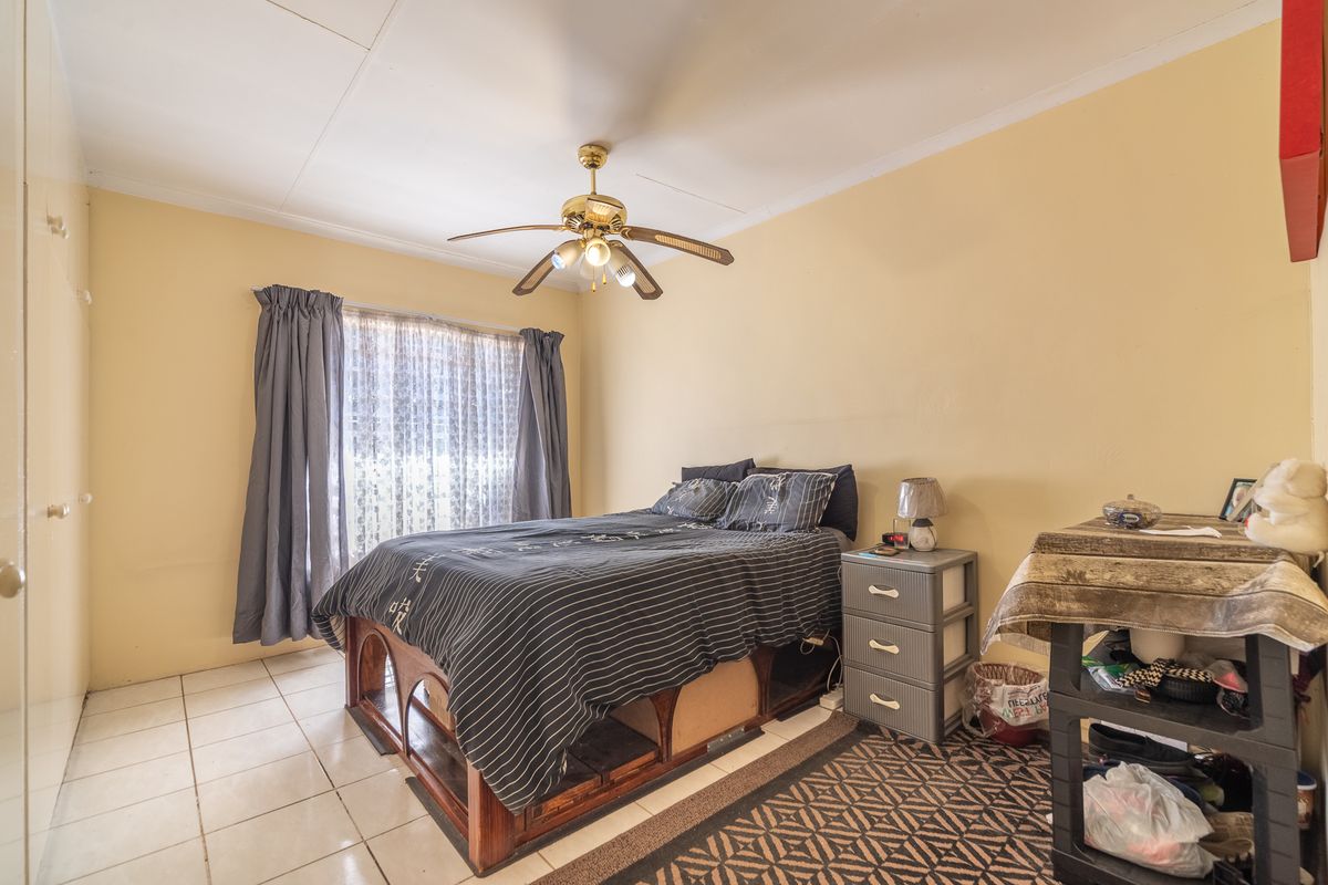 A functional bedroom featuring tiled flooring, a ceiling fan, and built-in cupboard storage.