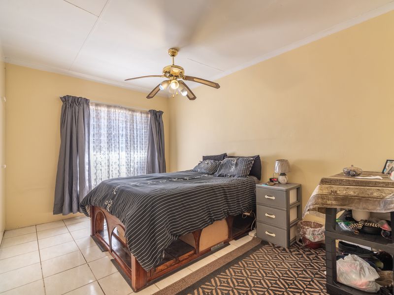 A functional bedroom featuring tiled flooring, a ceiling fan, and built-in cupboard storage.