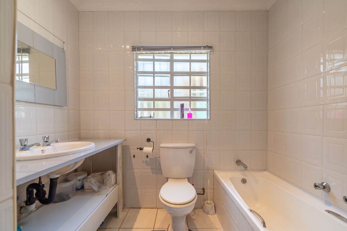 A functional bathroom featuring a built-in vanity, standard toilet, and bathtub with full-height wall tiling and a window with security bars.