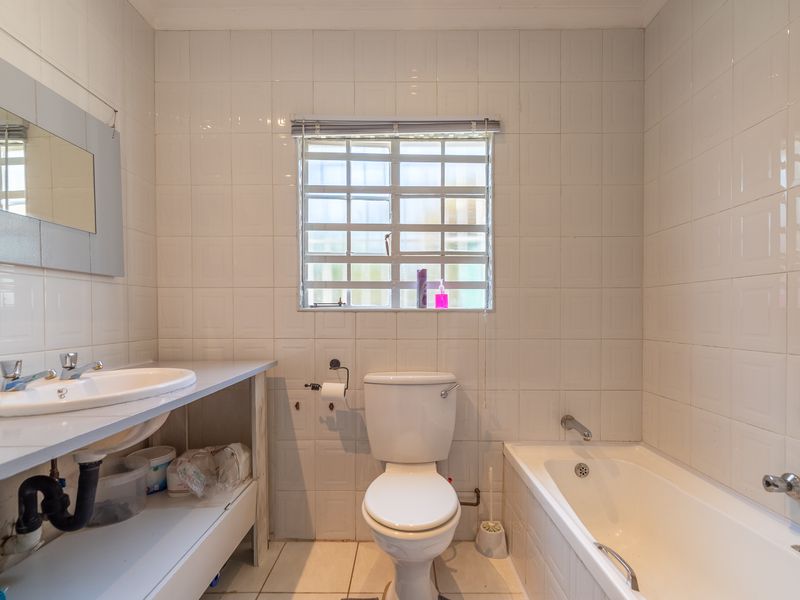 A functional bathroom featuring a built-in vanity, standard toilet, and bathtub with full-height wall tiling and a window with security bars.