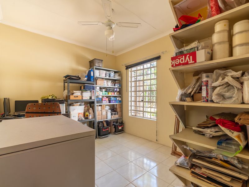 A functional utility or storage room featuring tiled flooring, a ceiling fan, and built-in shelving, with security bars installed on the window.