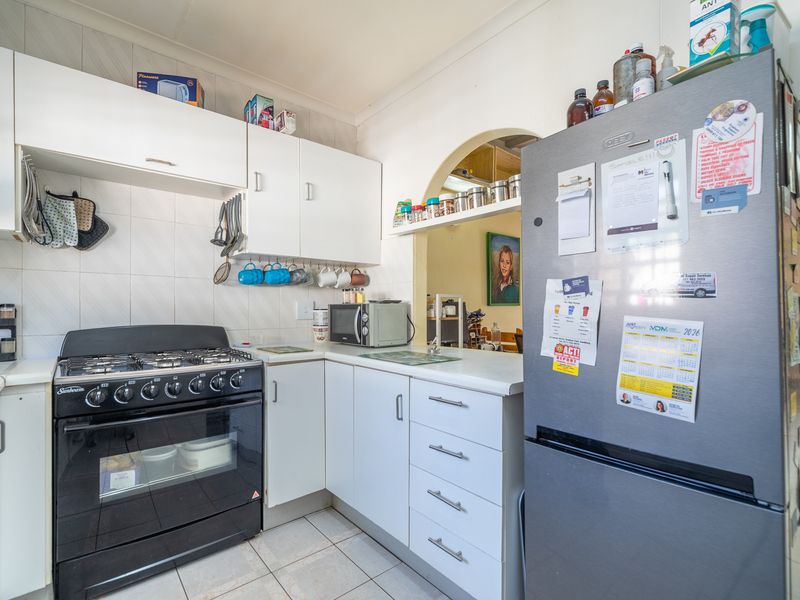 A functional kitchen featuring white cabinetry, a gas stove, and a tiled splashback, with an open archway connecting to the adjacent living space.