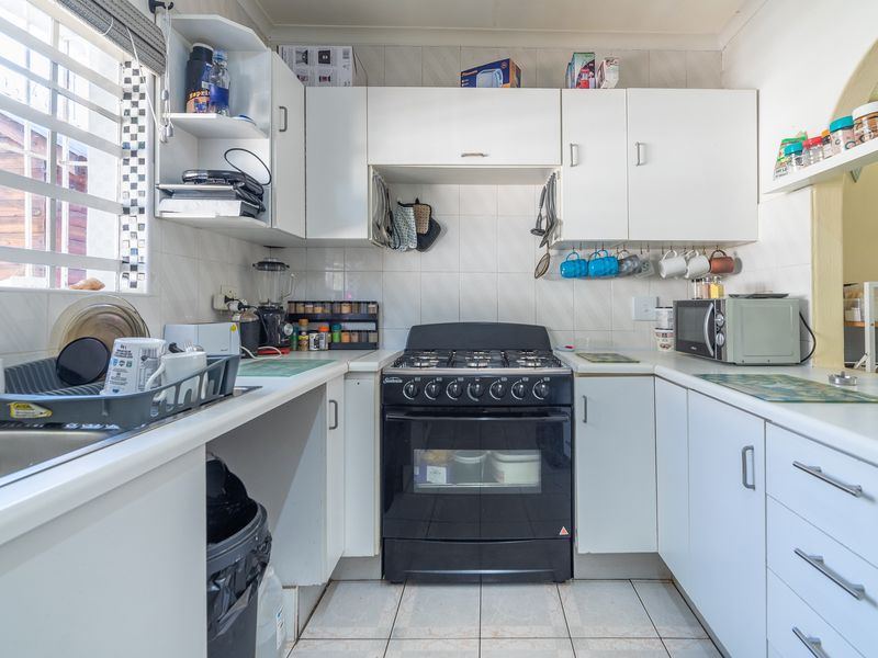 A functional kitchen featuring white cabinetry, laminate countertops, a gas stove, and tiled finishes, offering a practical layout for daily meal preparation.