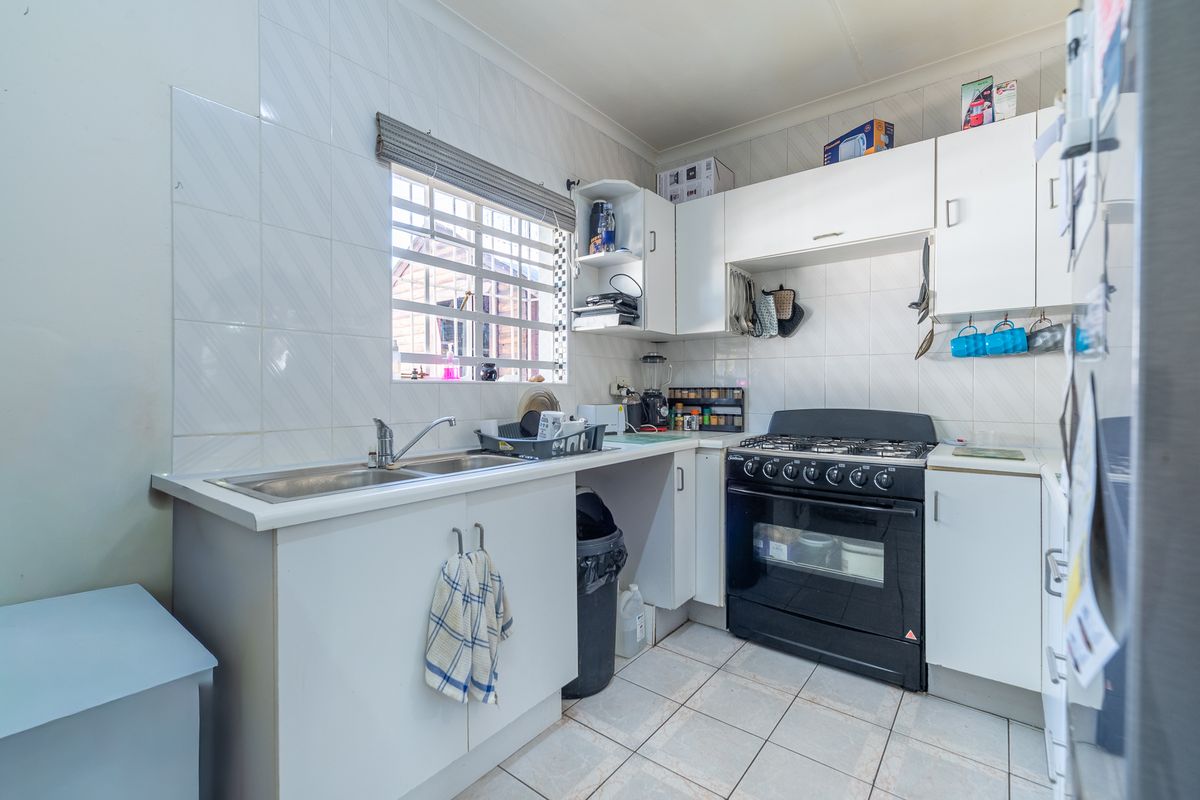 A functional kitchen featuring white cabinetry, tiled splashbacks, a gas stove with oven, and a stainless steel sink.