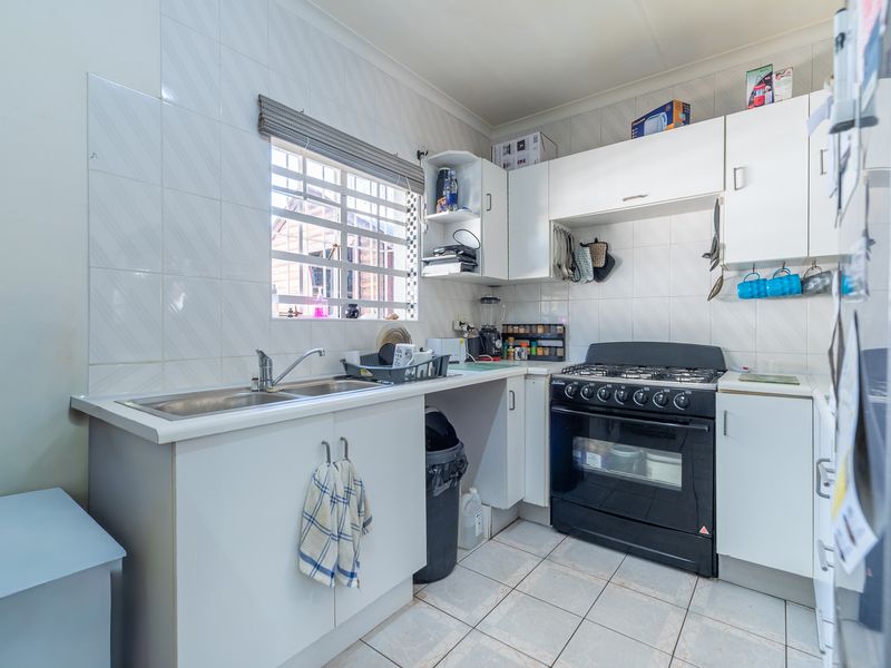 A functional kitchen featuring white cabinetry, tiled splashbacks, a gas stove with oven, and a stainless steel sink.