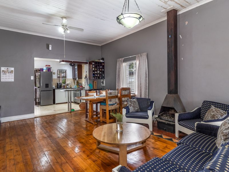Open-plan living and dining area featuring original timber flooring, a freestanding fireplace, and a connected kitchen space with a rustic timber ceiling.