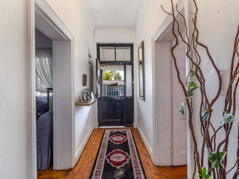 A traditional hallway featuring original timber flooring, high ceilings with cornicing, and a classic timber entrance door leading to the exterior.