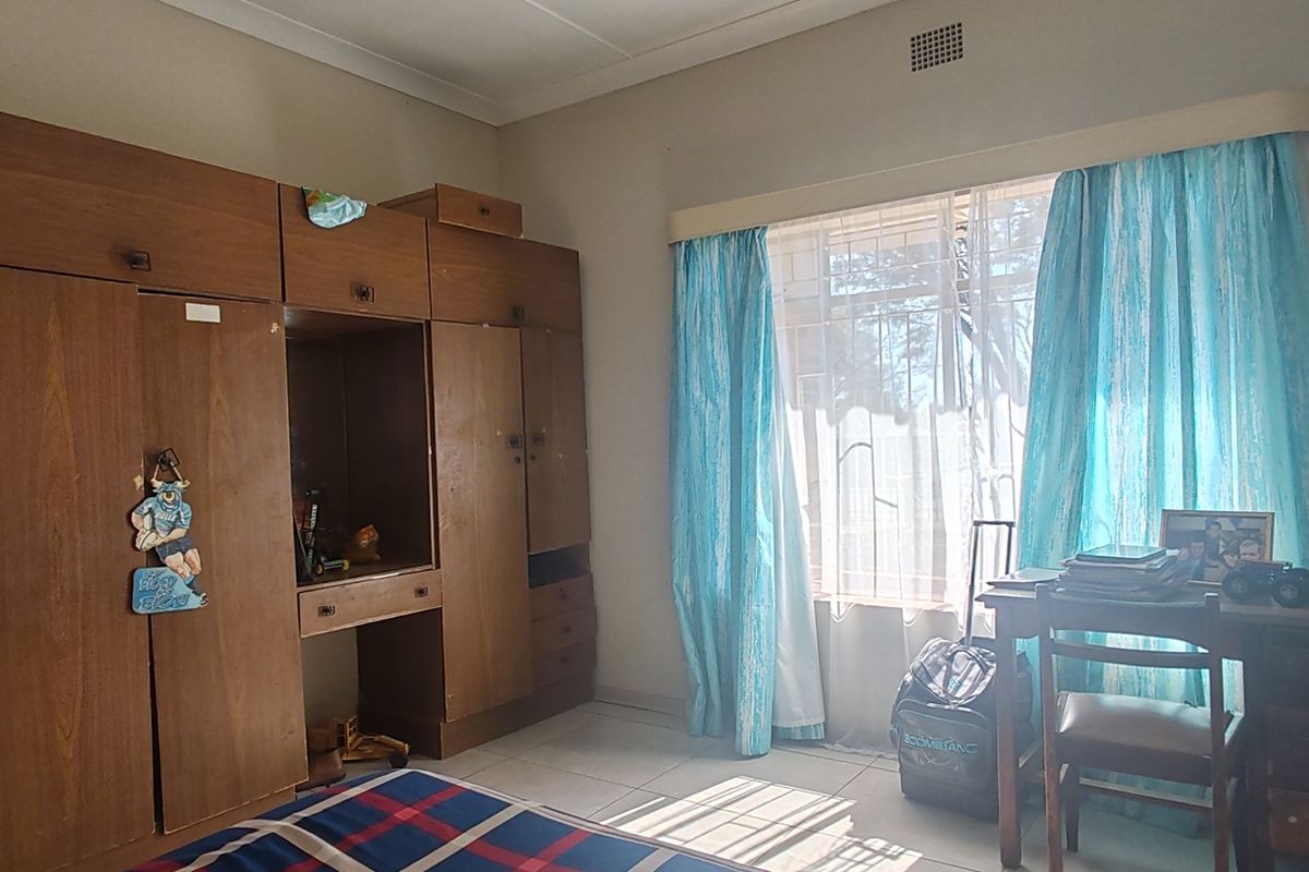 A bedroom featuring built-in wooden cupboards, tiled flooring, and a window fitted with security bars.