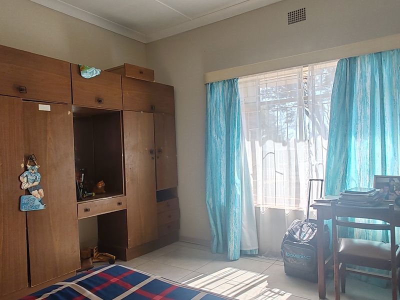 A bedroom featuring built-in wooden cupboards, tiled flooring, and a window fitted with security bars.