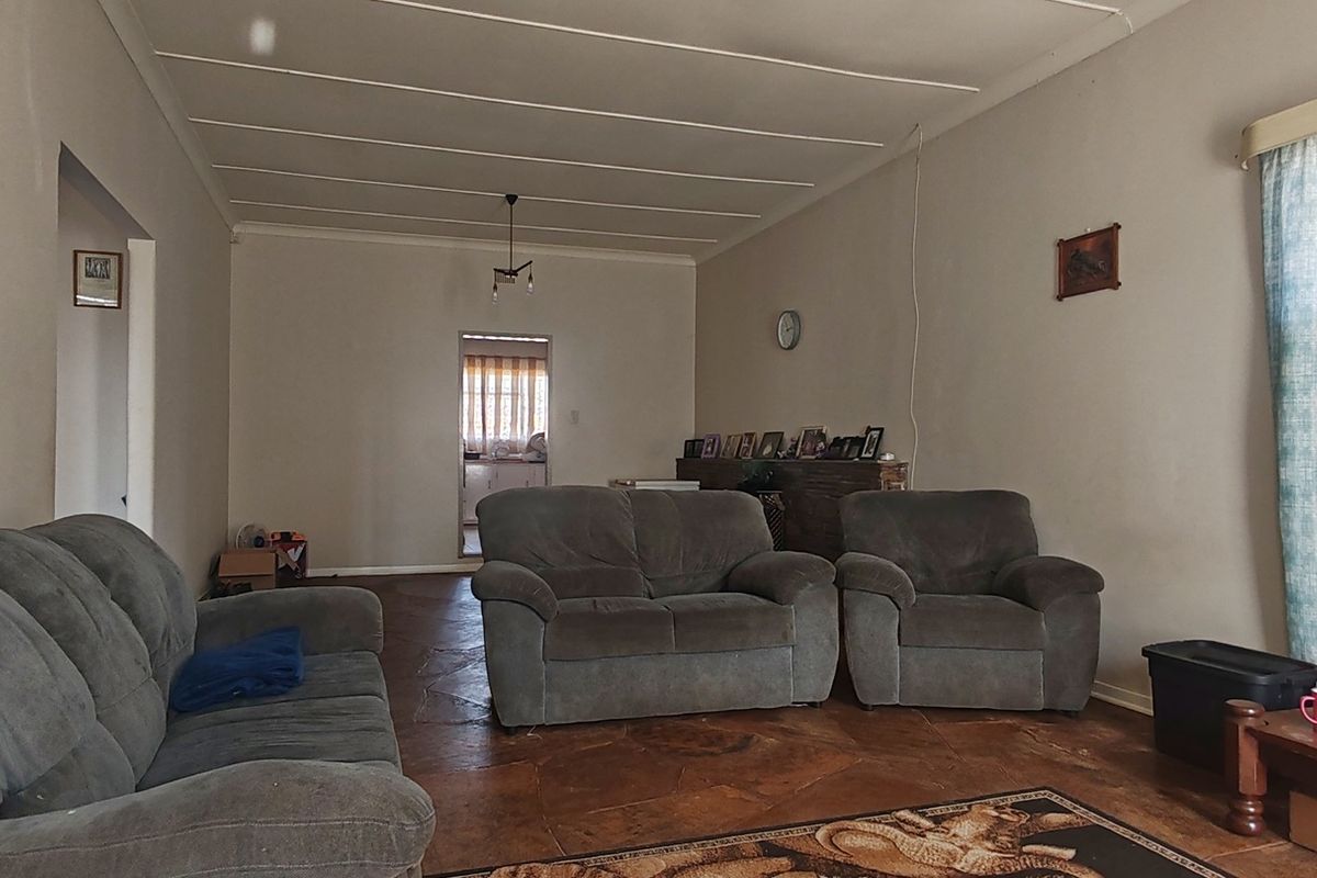 A living room featuring tiled flooring and a coved ceiling, showing signs of wear and requiring cosmetic updates.