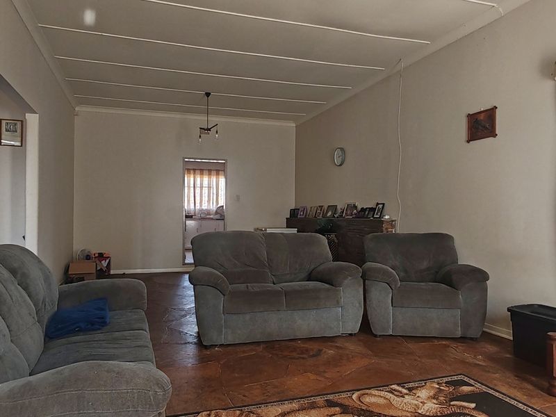 A living room featuring tiled flooring and a coved ceiling, showing signs of wear and requiring cosmetic updates.