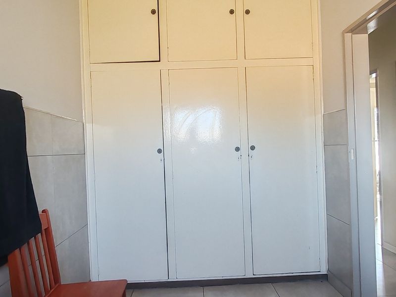 A hallway featuring built-in floor-to-ceiling storage cupboards, tiled flooring, and tiled wall wainscoting.