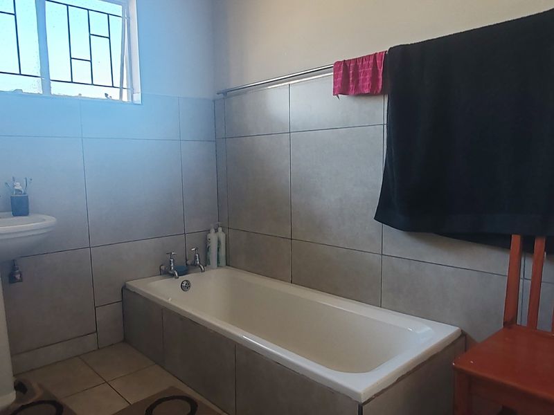 A functional bathroom featuring a pedestal basin, a built-in bathtub, and neutral wall tiling with security bars on the window.